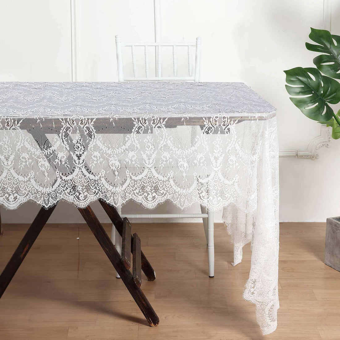Lace tablecloth draped over a wooden table with a chair and plant in the background.