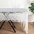 Lace tablecloth draped over a wooden table with a chair and plant in the background.